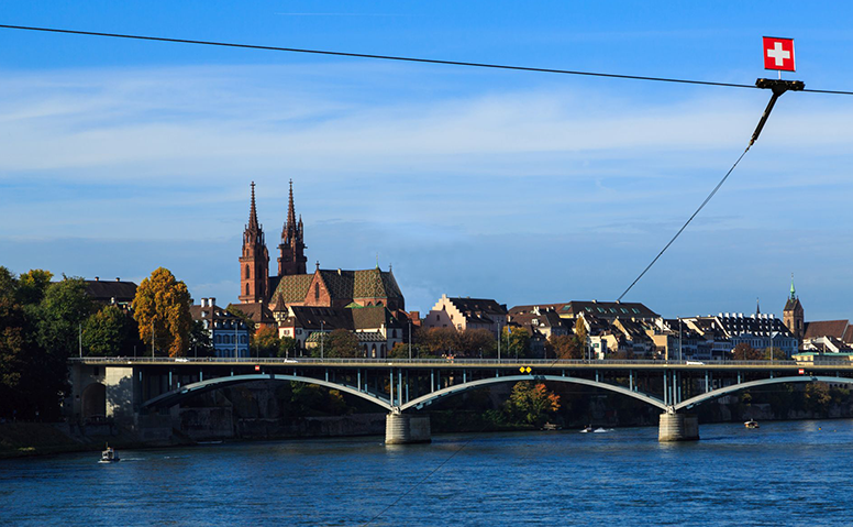 Switzerland: Panoramic view of the old town of Basel, looking across the River Rhine to a bridge, Swiss flag top right 