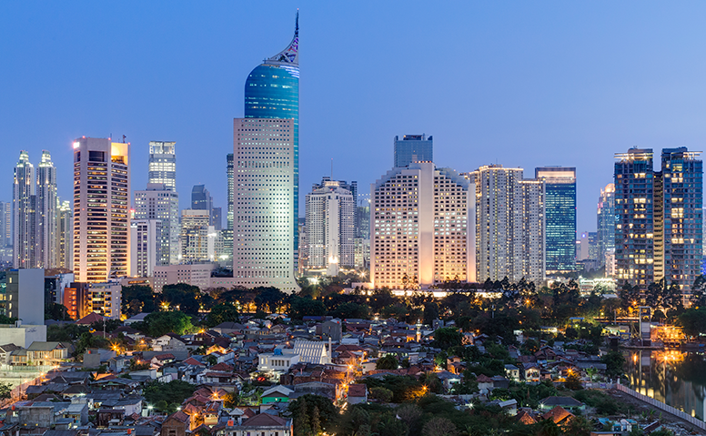 Indonesia: Shot of Jakarta at dusk, small houses with trees silhouetted against the skyline of large skyscrapers