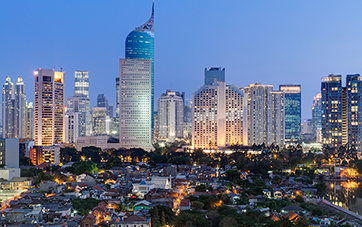 Indonesia: Shot of Jakarta at dusk, small houses with trees silhouetted against the skyline of large skyscrapers